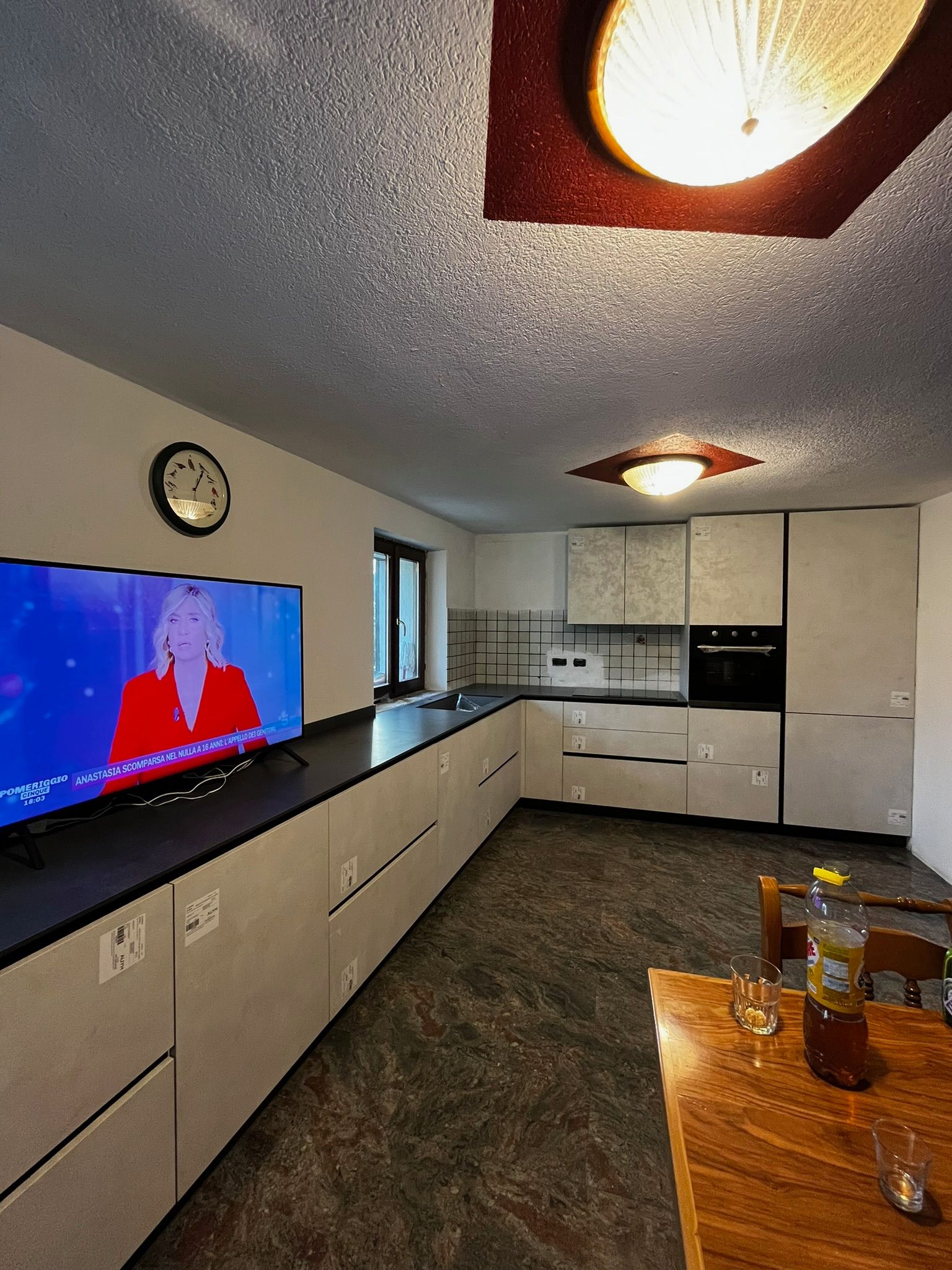 Cucina moderna con zona pranzo, mobili bianchi, piani di lavoro scuri, TV a parete e tavolo in legno