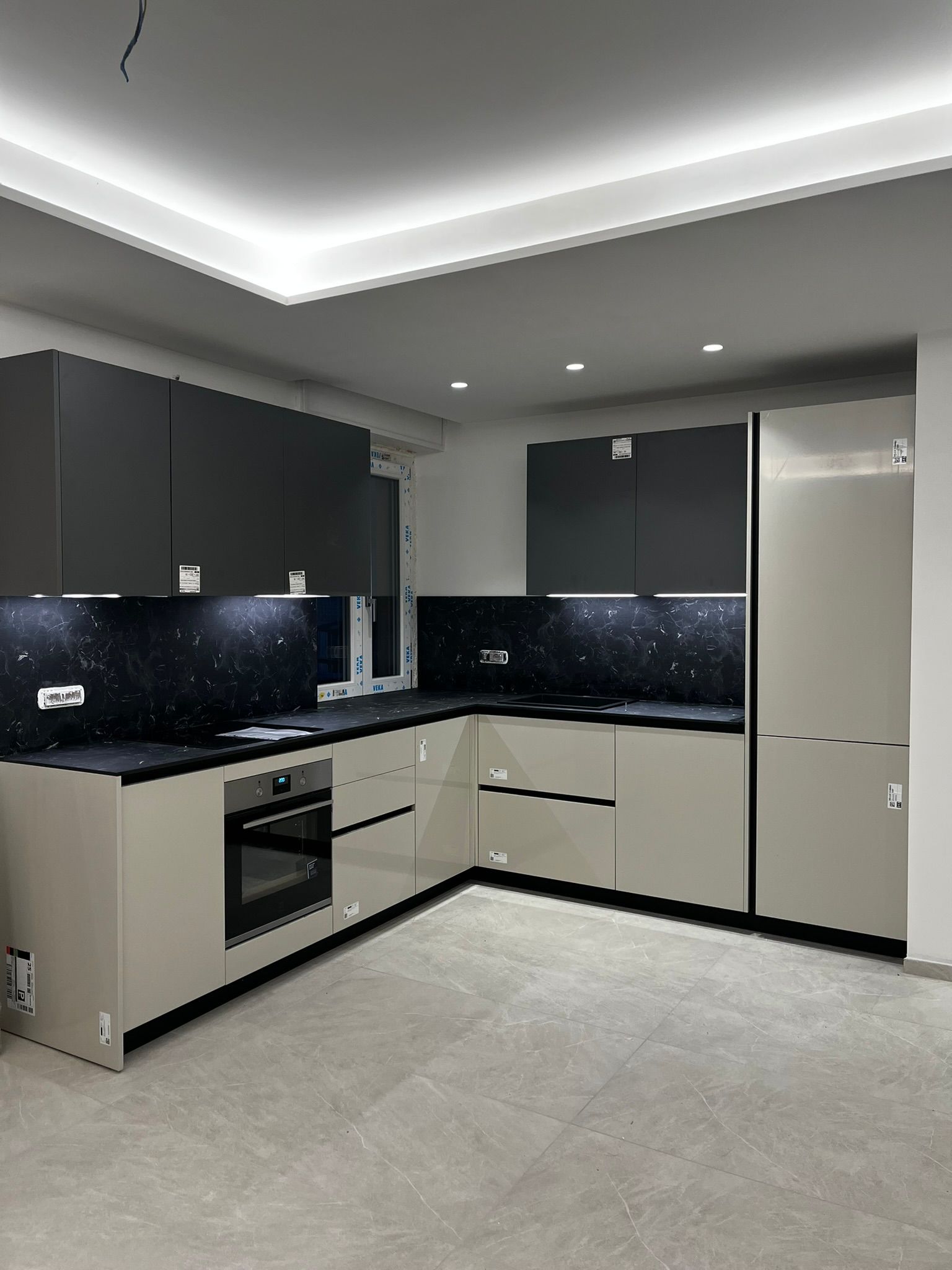 Cucina moderna grigia con piani di lavoro neri, paraschizzi lucido, forno da incasso e frigorifero alto, con luci LED a soffitto