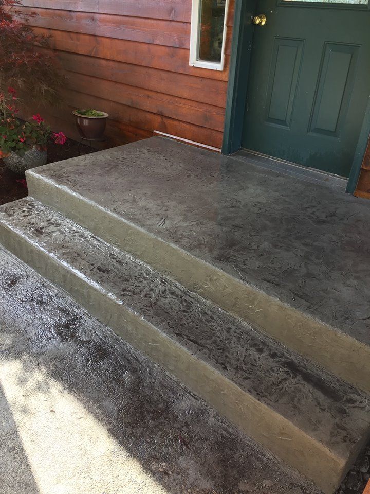 Concrete front steps leading to a green door beside a wooden exterior wall