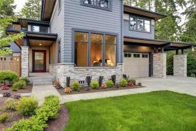 Modern two-story gray house with front lawn, stone walkway, and warm-lit windows
