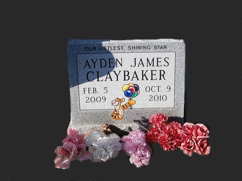 Memorial plaque for Aydn James Claybaker with flowers and a trinket at the base