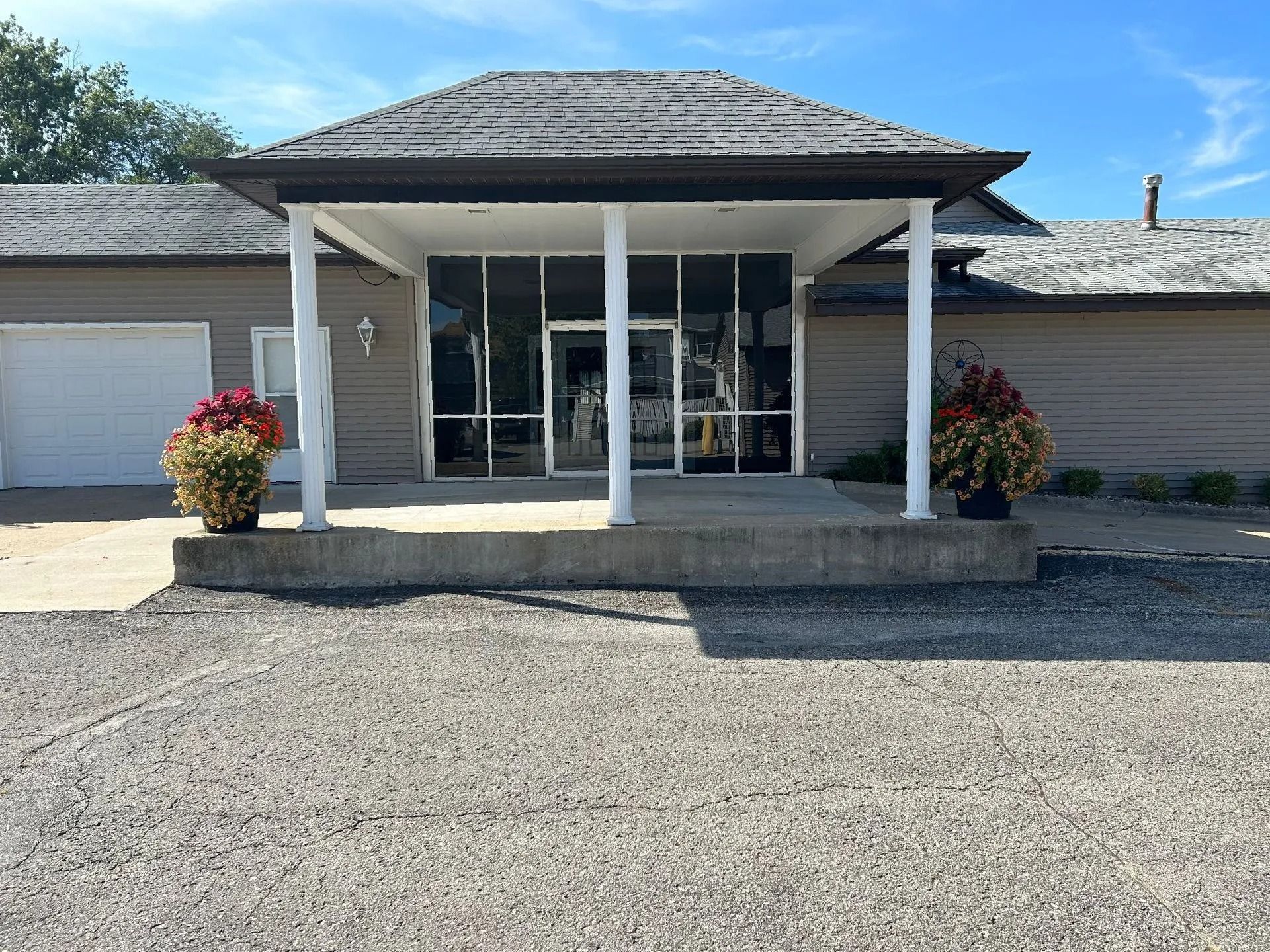 Front entrance of a building with white columns, glass doors, and flower planters in front
