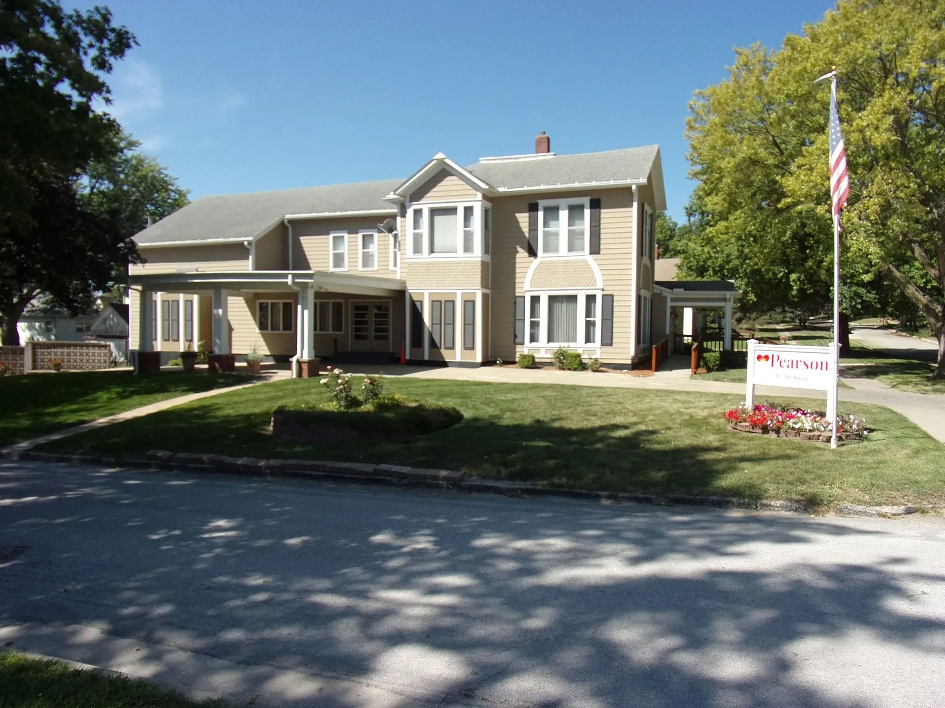 Two-story beige house with white trim and a front lawn, seen from the street on a sunny day.