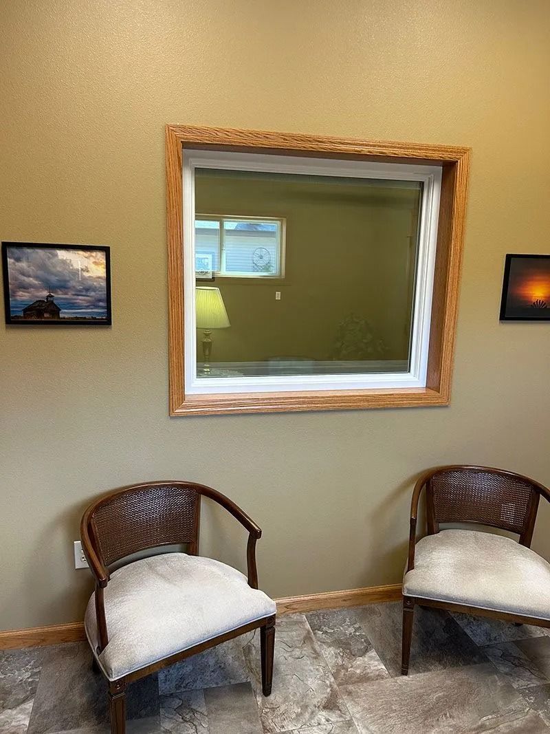 Waiting area with two wicker chairs, a large wall mirror, and small framed landscape art on beige walls.