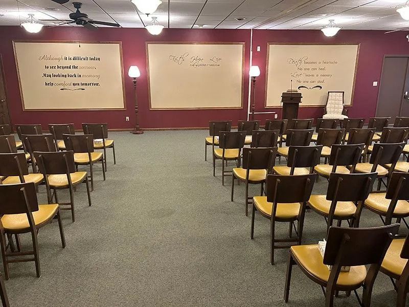 Empty lecture hall with rows of chairs facing a maroon front wall and whiteboards.