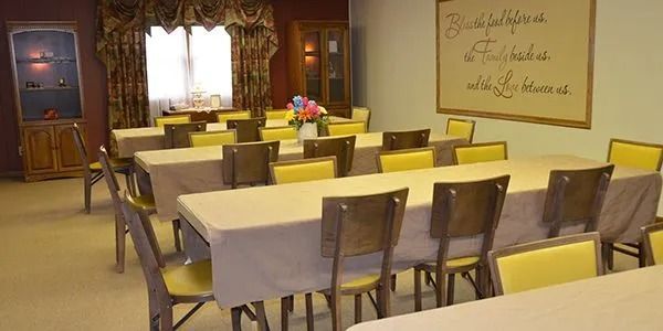 Empty banquet room with yellow chairs and white tablecloths, lit by a window and wall decor