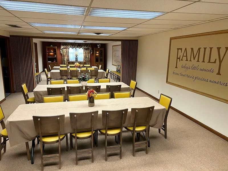 Meeting room with long tables, yellow chairs, and a wall sign reading “FAMILY.”