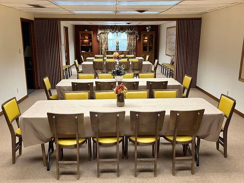Dining room with long tables, yellow chairs, and neatly set place settings in a formal banquet space