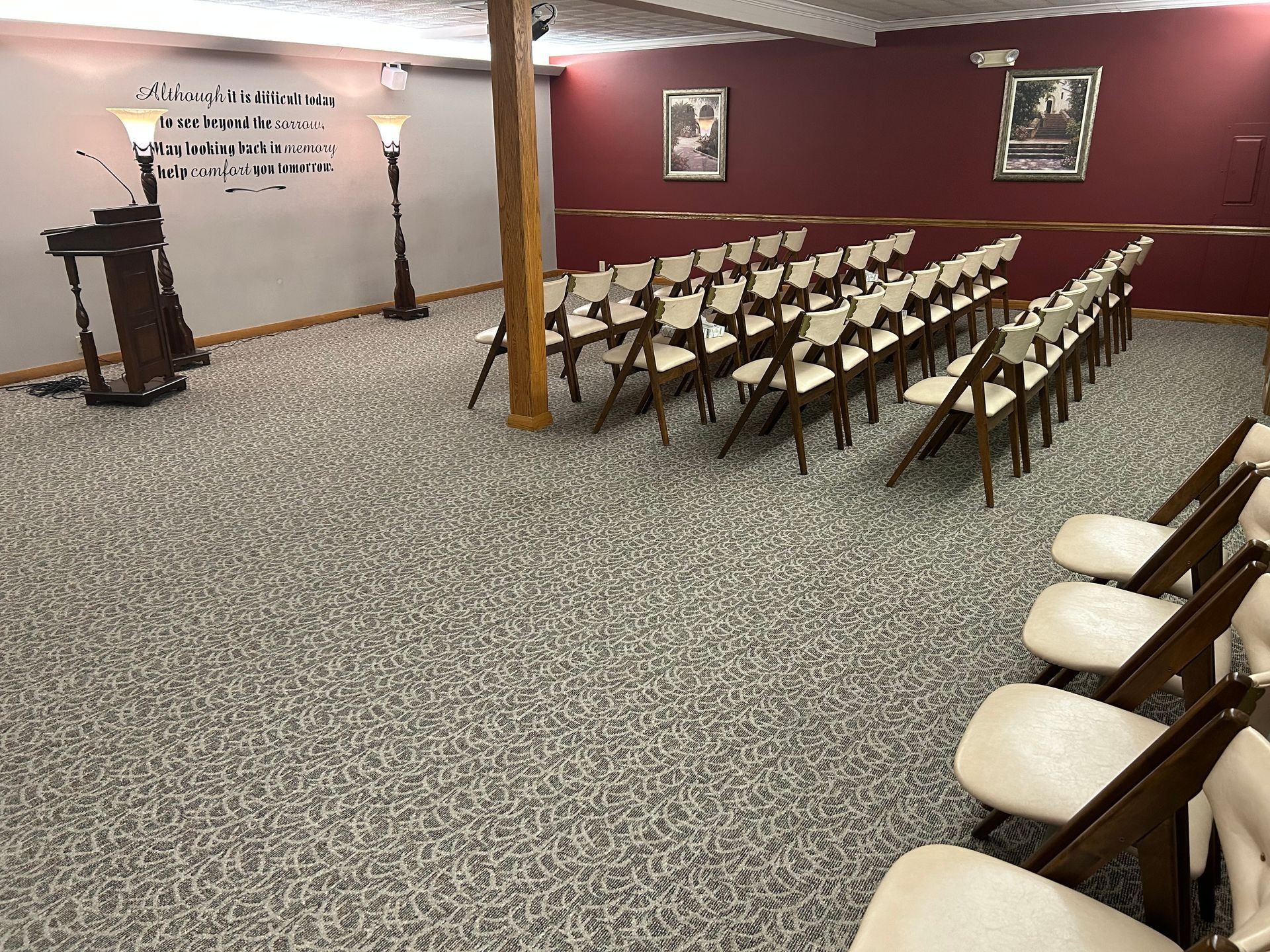 Empty lecture hall with rows of folding chairs, a podium, and maroon walls with framed portraits.