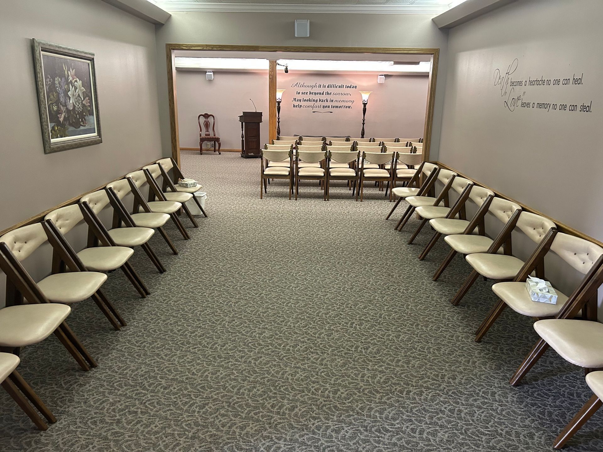 Empty church chapel with rows of chairs facing a lit altar and podium, white walls, and carpeted floor