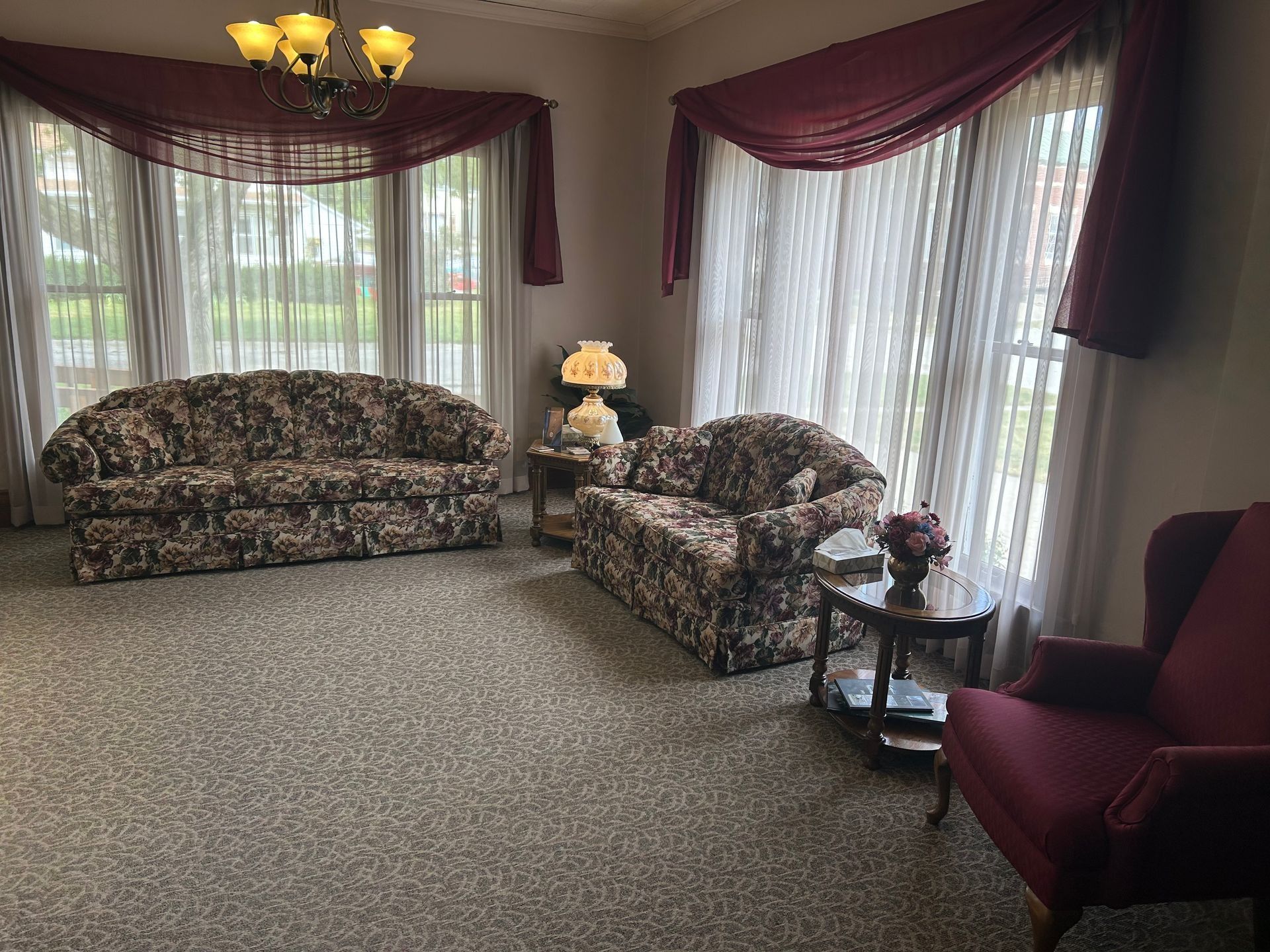 Floral living room with sofa, armchairs, and large windows with burgundy drapes