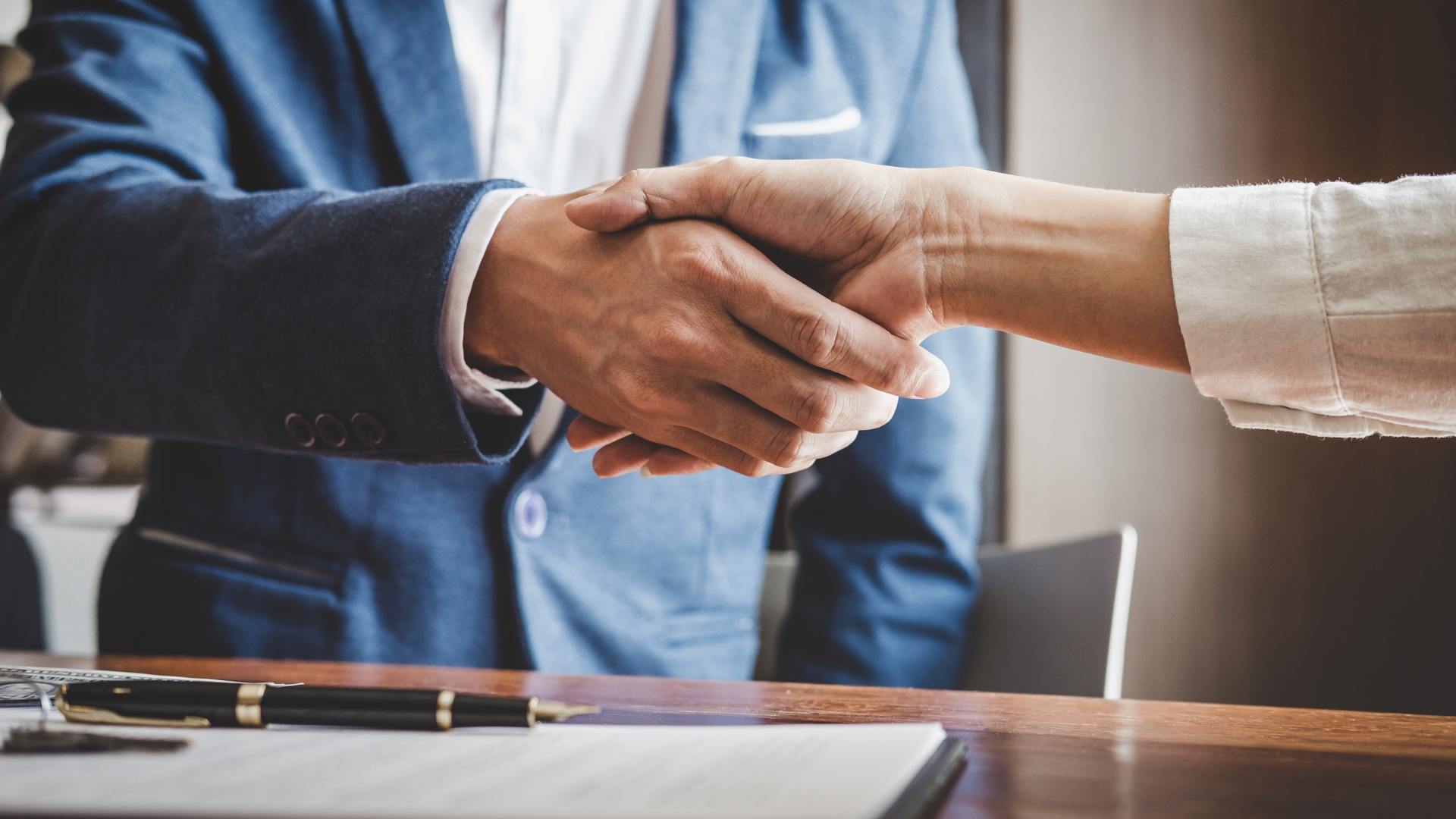 Two people shaking hands across a desk in an office setting