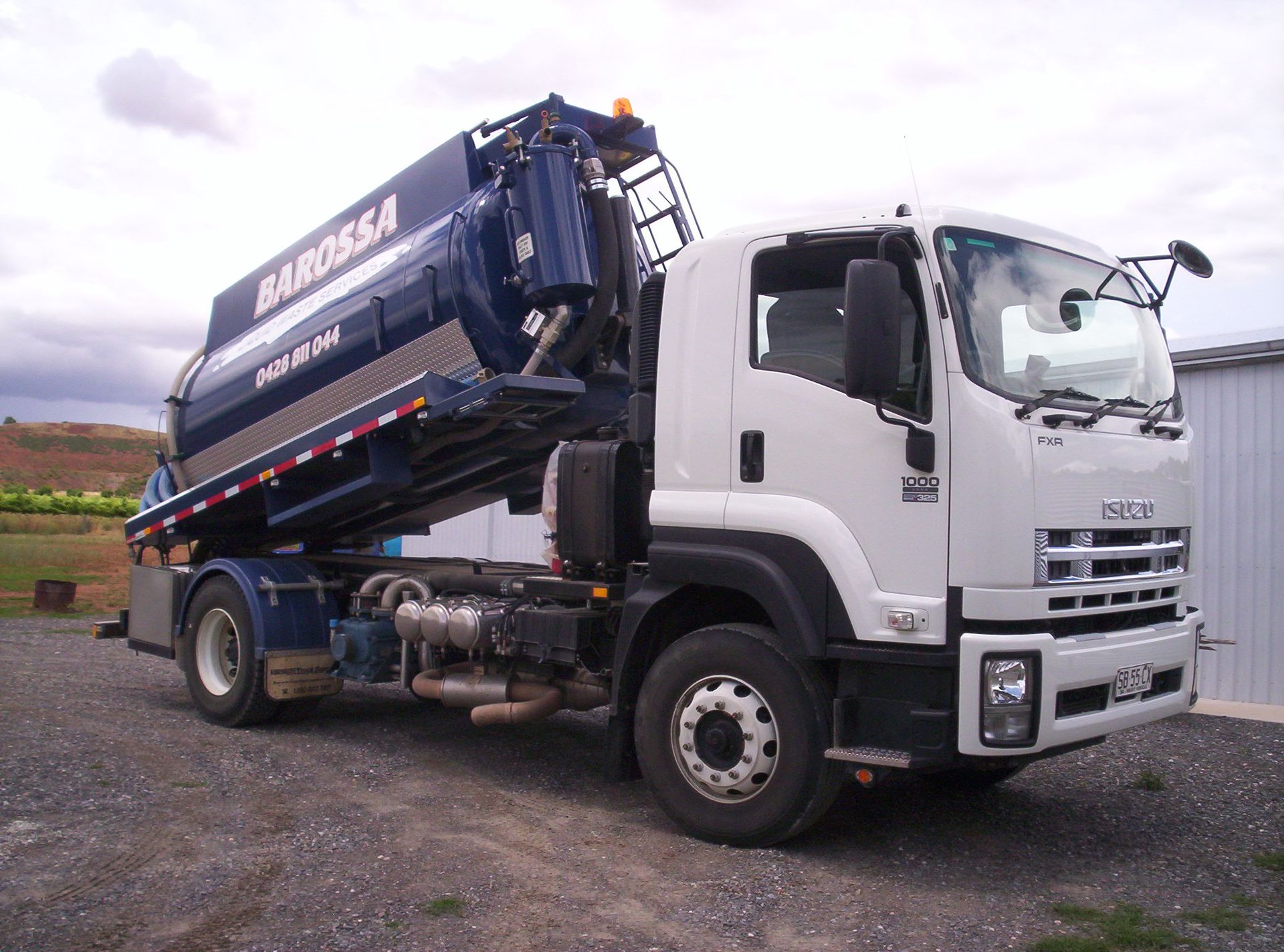 White and blue vacuum truck; parked outdoors. The truck has a large dark blue tank with the name 