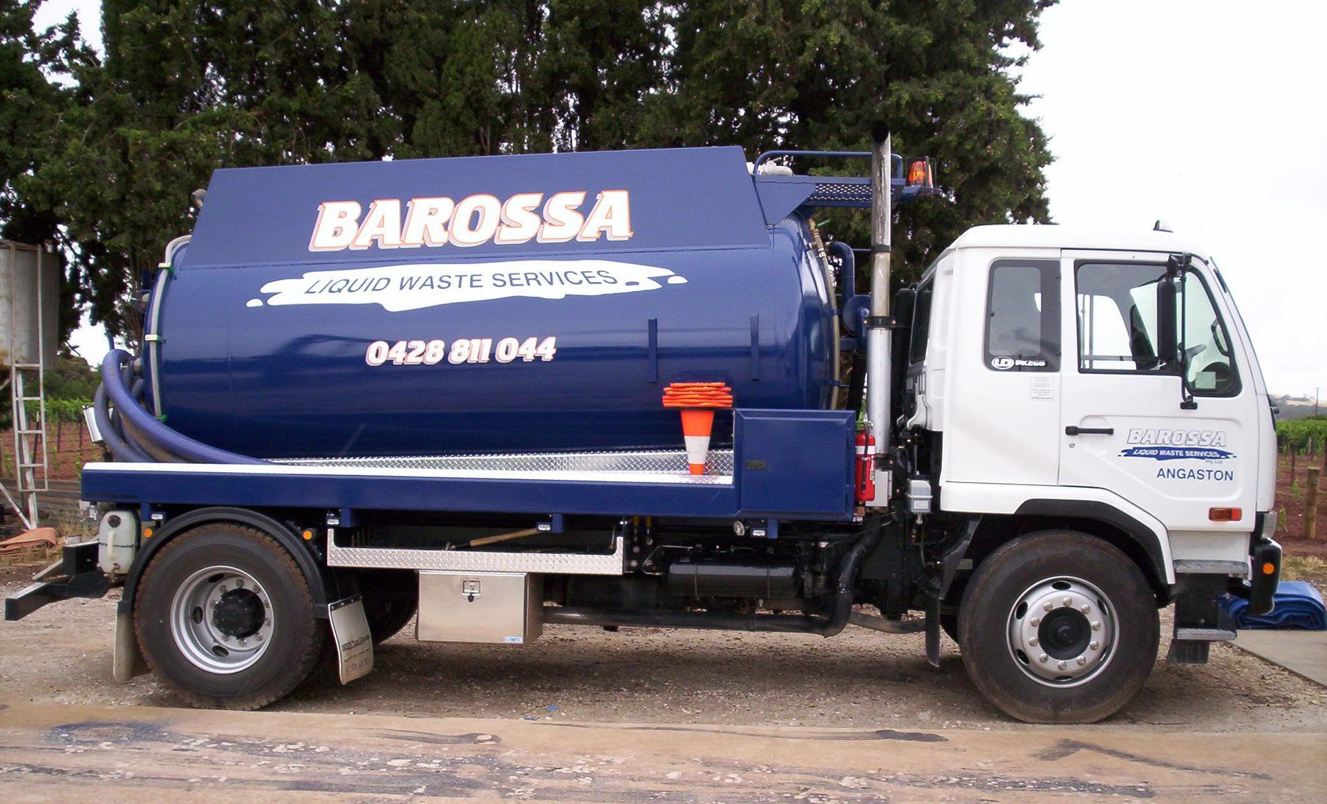 Blue and white Barossa waste removal truck with a large tank parked outside.