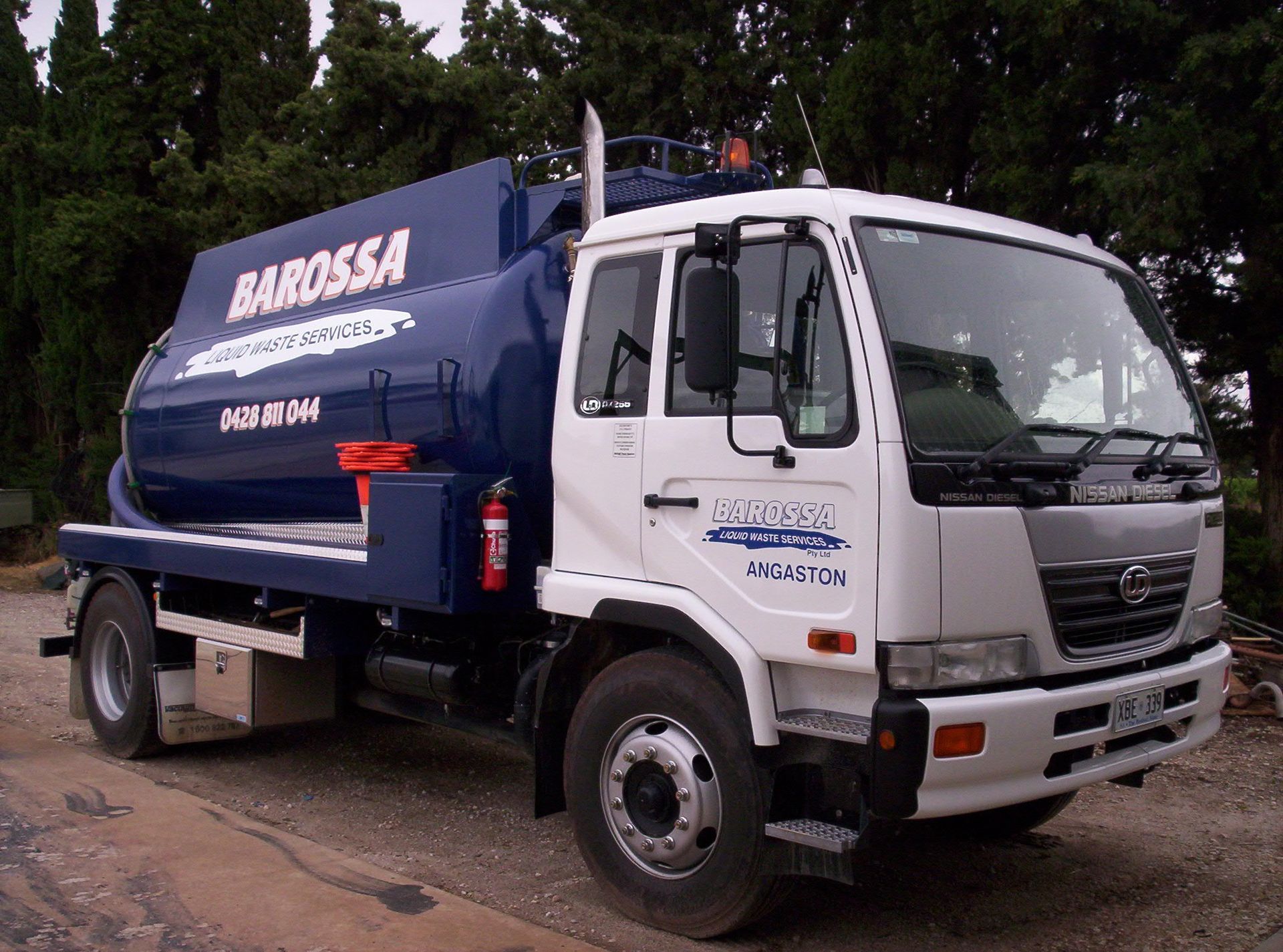 A white and blue Barossa Industries vacuum truck on a road with trees in the background.