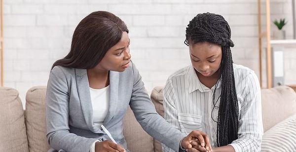 Two women sit on a couch, one offering guidance as they look at a document together.