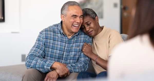 Two people smiling and leaning together on a couch in a bright living room