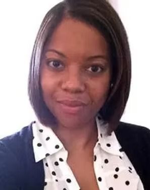 Head-and-shoulders portrait of a smiling woman in a white polka-dot blouse and black blazer.