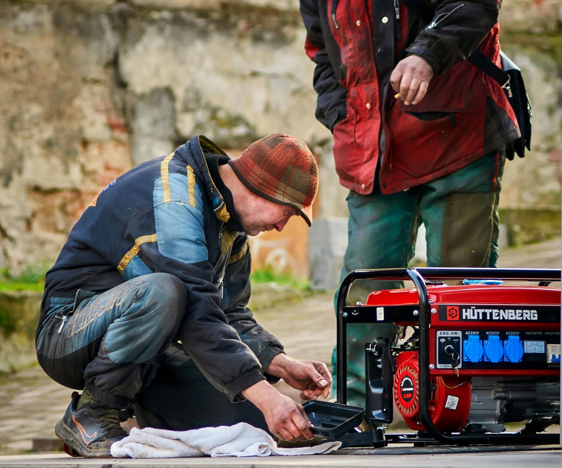 Two people set up a red generator outdoors, with one kneeling beside cables and tools