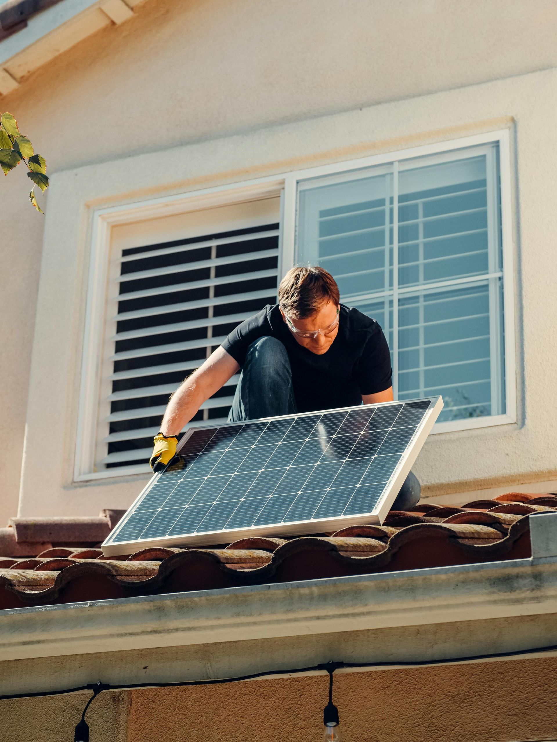 Worker installing a solar panel on a house roof beside a window