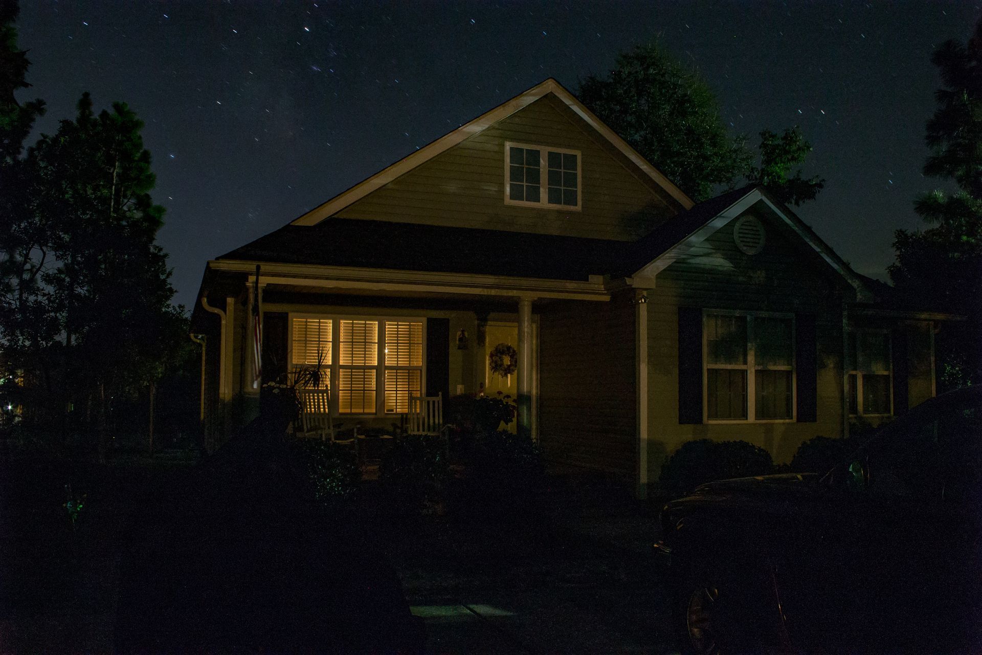 A house at night with lights on, stars visible in the sky.