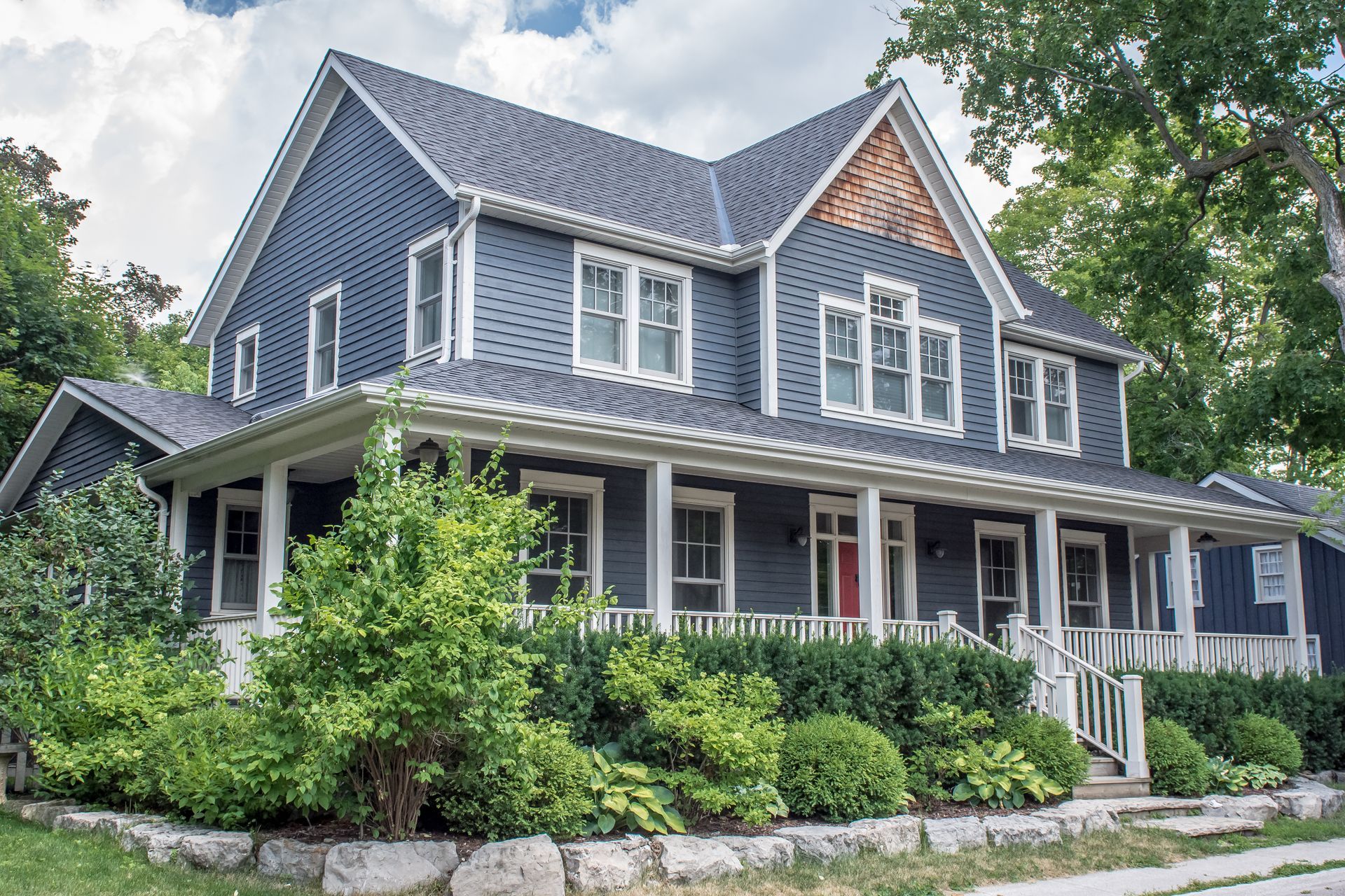 Blue house with white trim, front porch, and lush green landscaping.