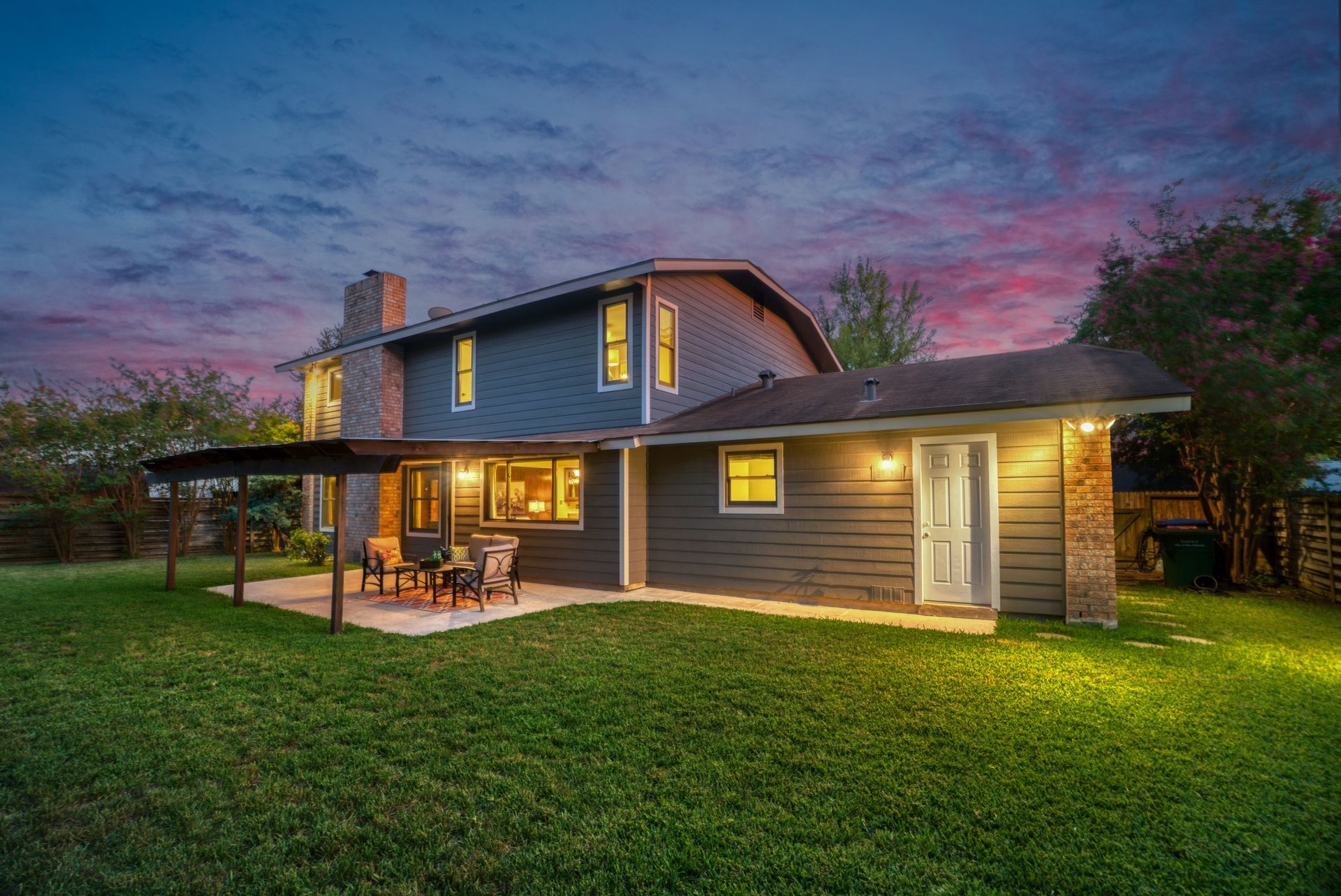 House with lit porch and yard at dusk under a colorful sky