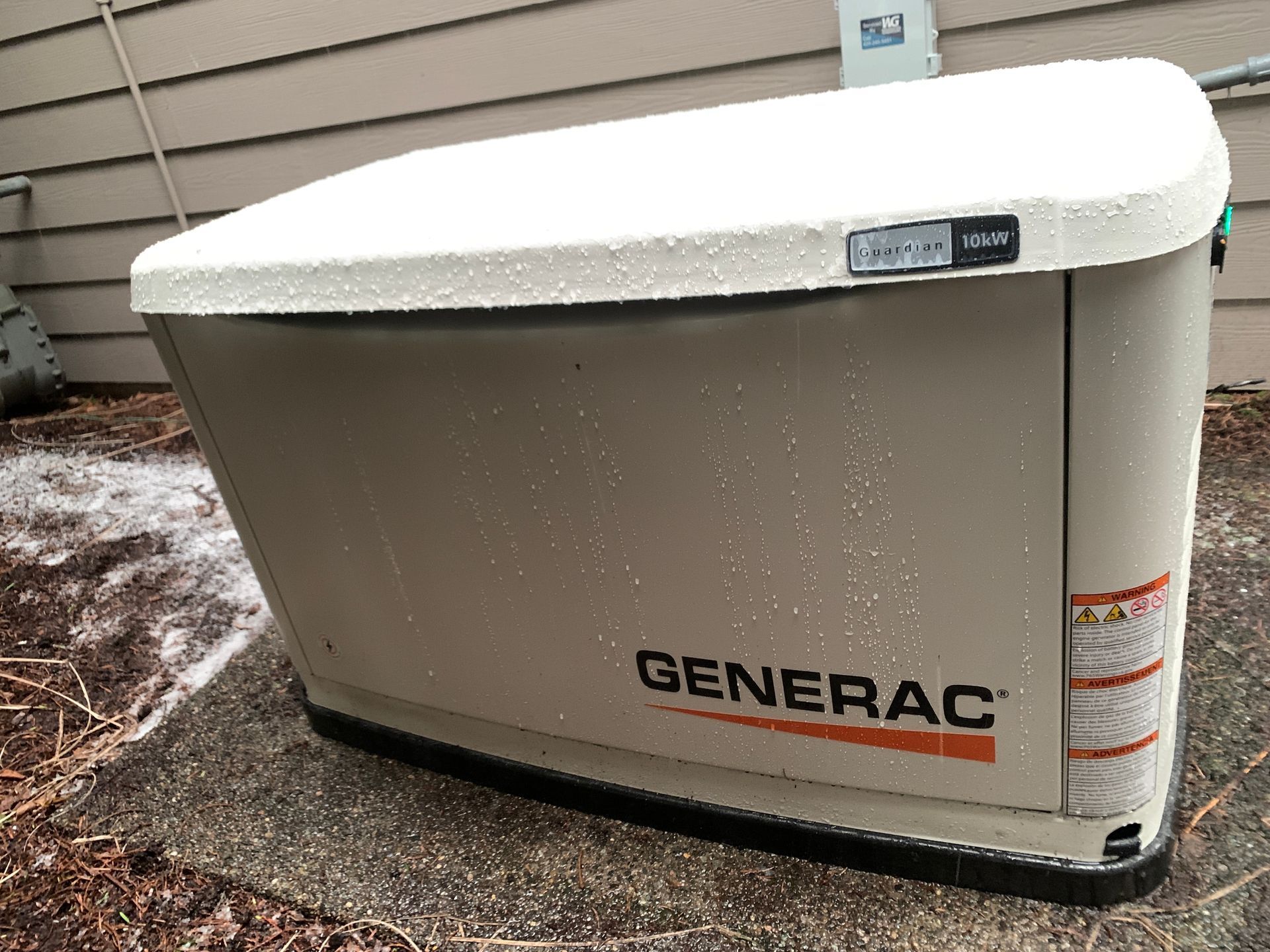 Generac home standby generator beside a house, white and gray unit on a gravel patch.