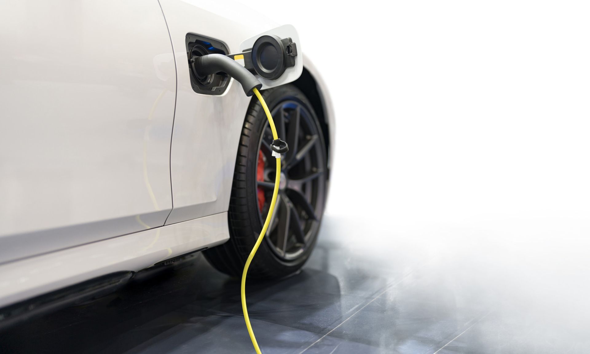 White electric car charging with a yellow cable at a wall charger near the front wheel