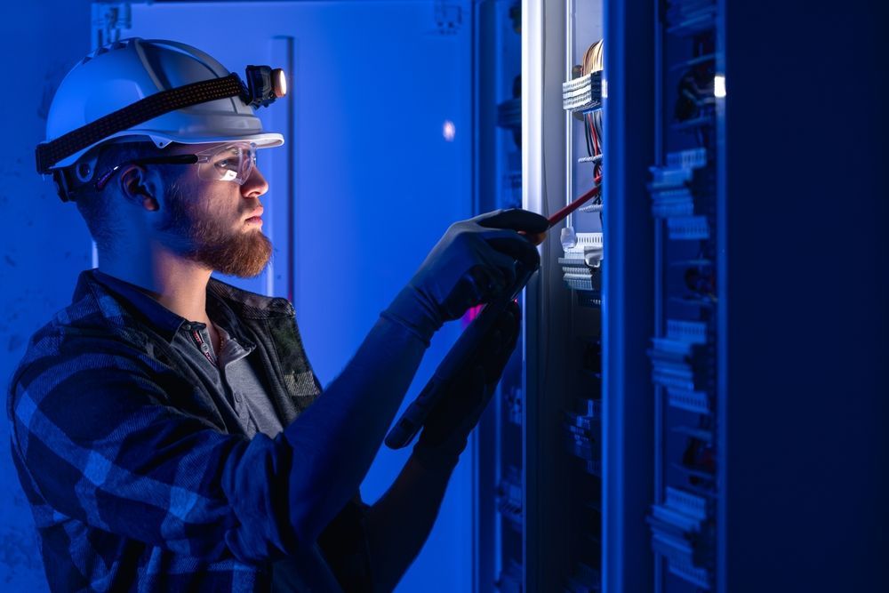Technician in hard hat and glasses inspecting server racks in blue-lit data center