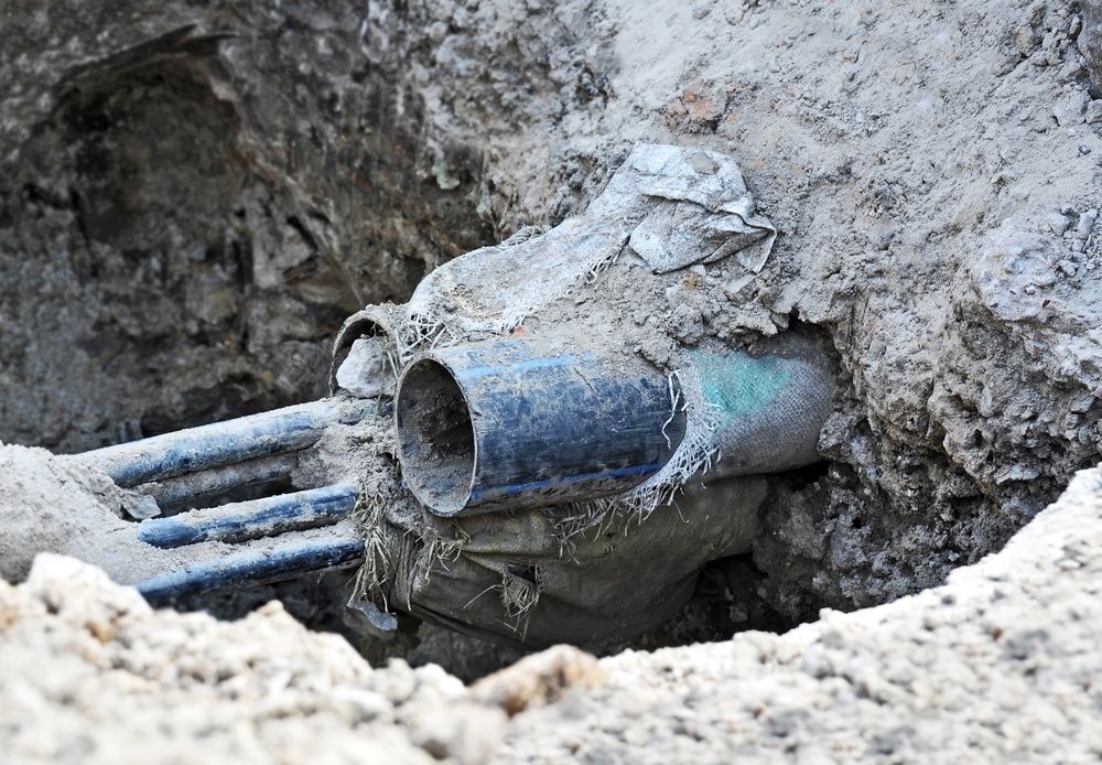 Exposed blue pipes and a pipe joint in a dirt trench during excavation