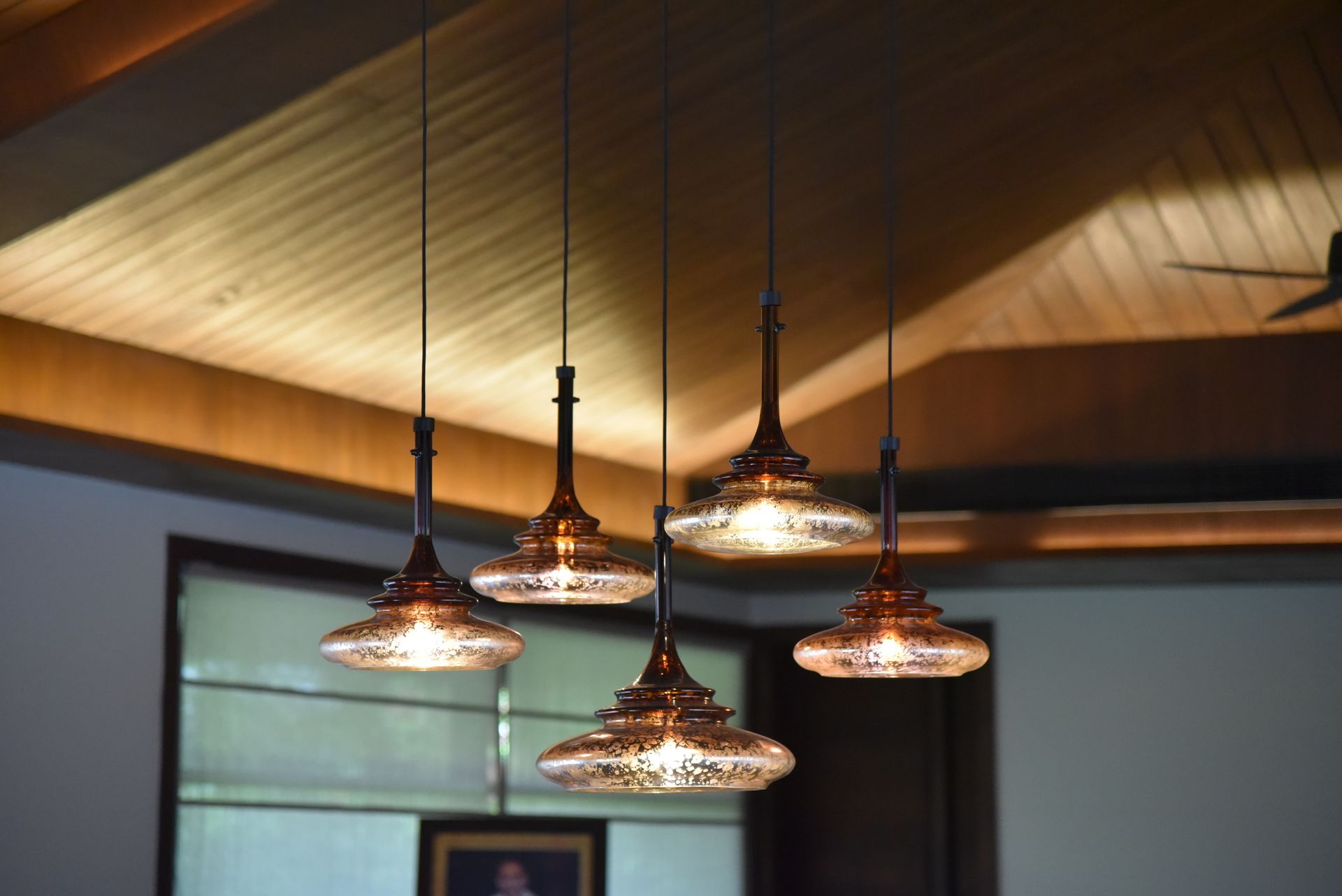 Five hanging pendant lights with warm glow under a wood ceiling in a modern room
