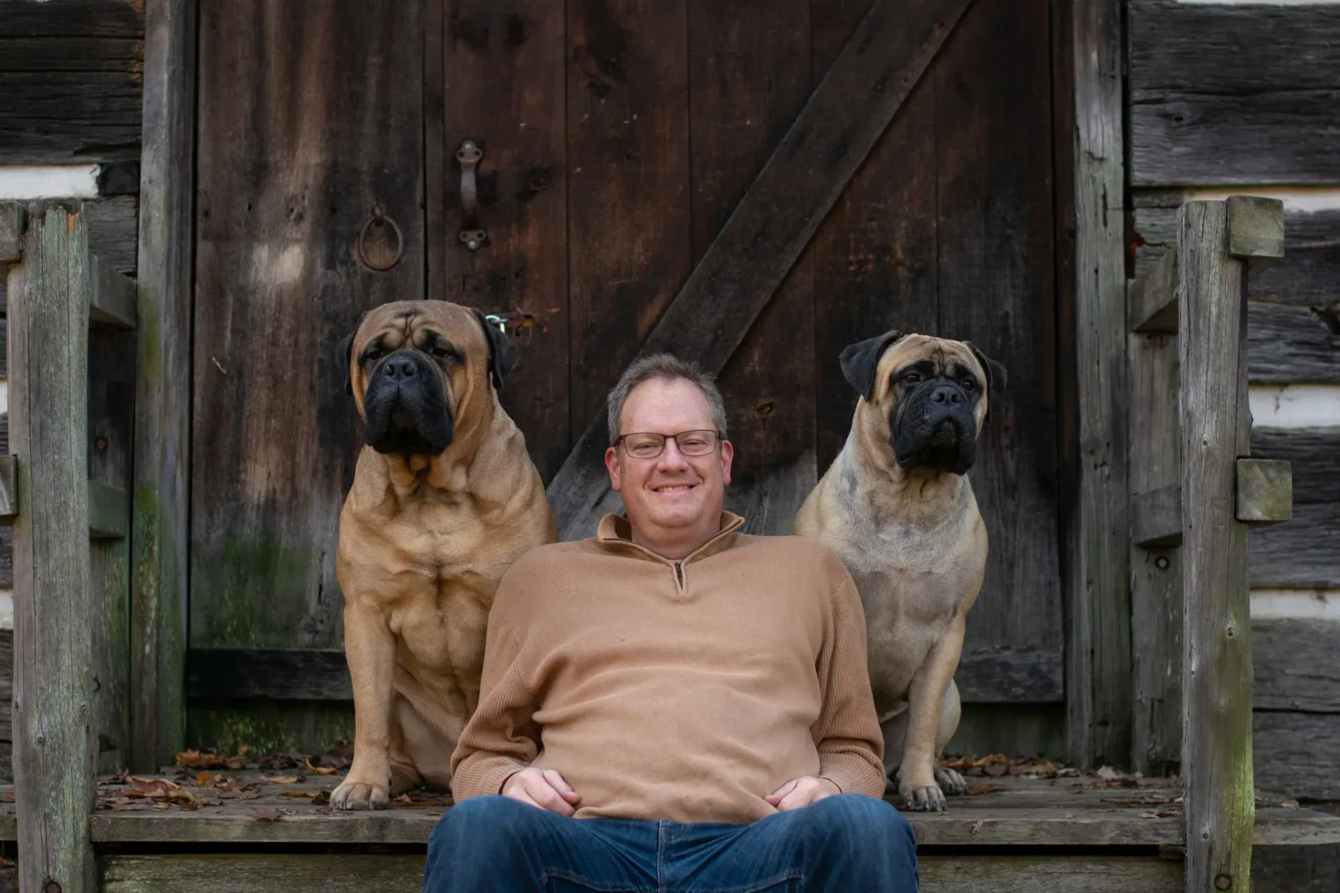 A man sits on a porch with two dogs