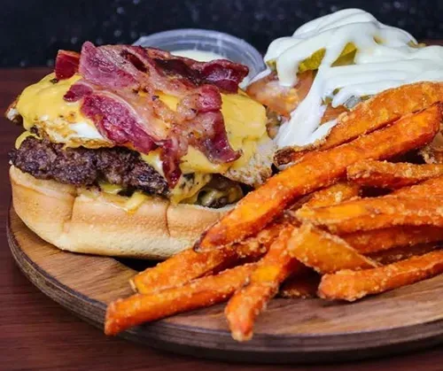 A hamburger and sweet potato fries on a wooden cutting board.