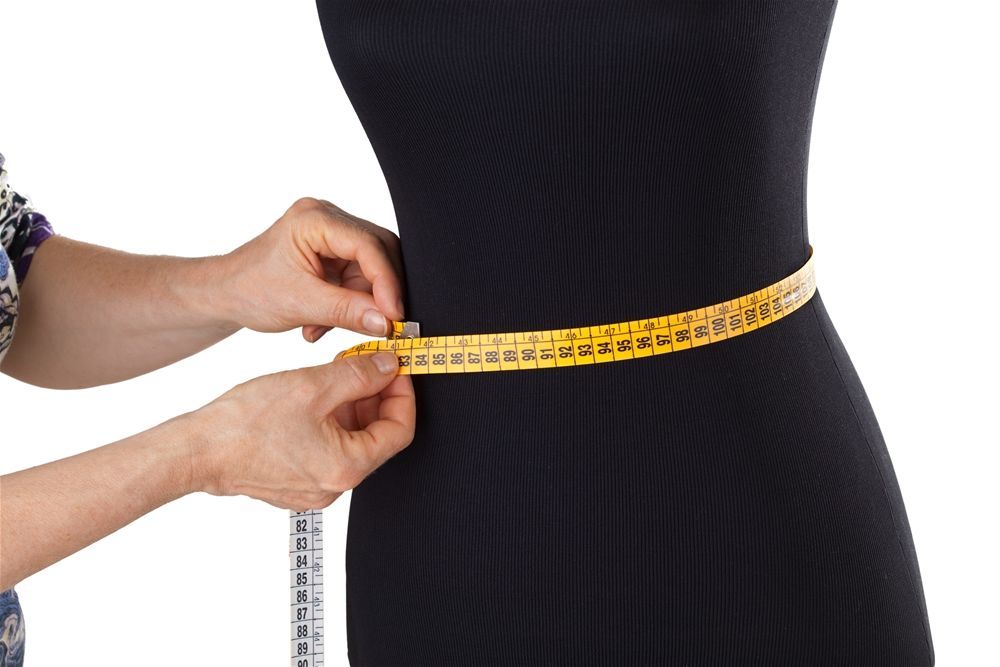 A woman is measuring a mannequin 's waist with a tape measure