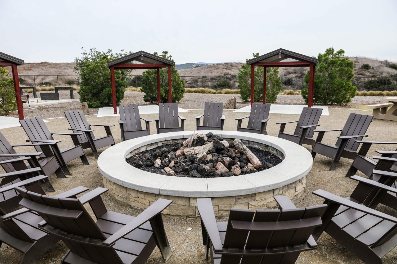 Outdoor fire pit surrounded by gray lounge chairs and pergolas in a desert resort courtyard