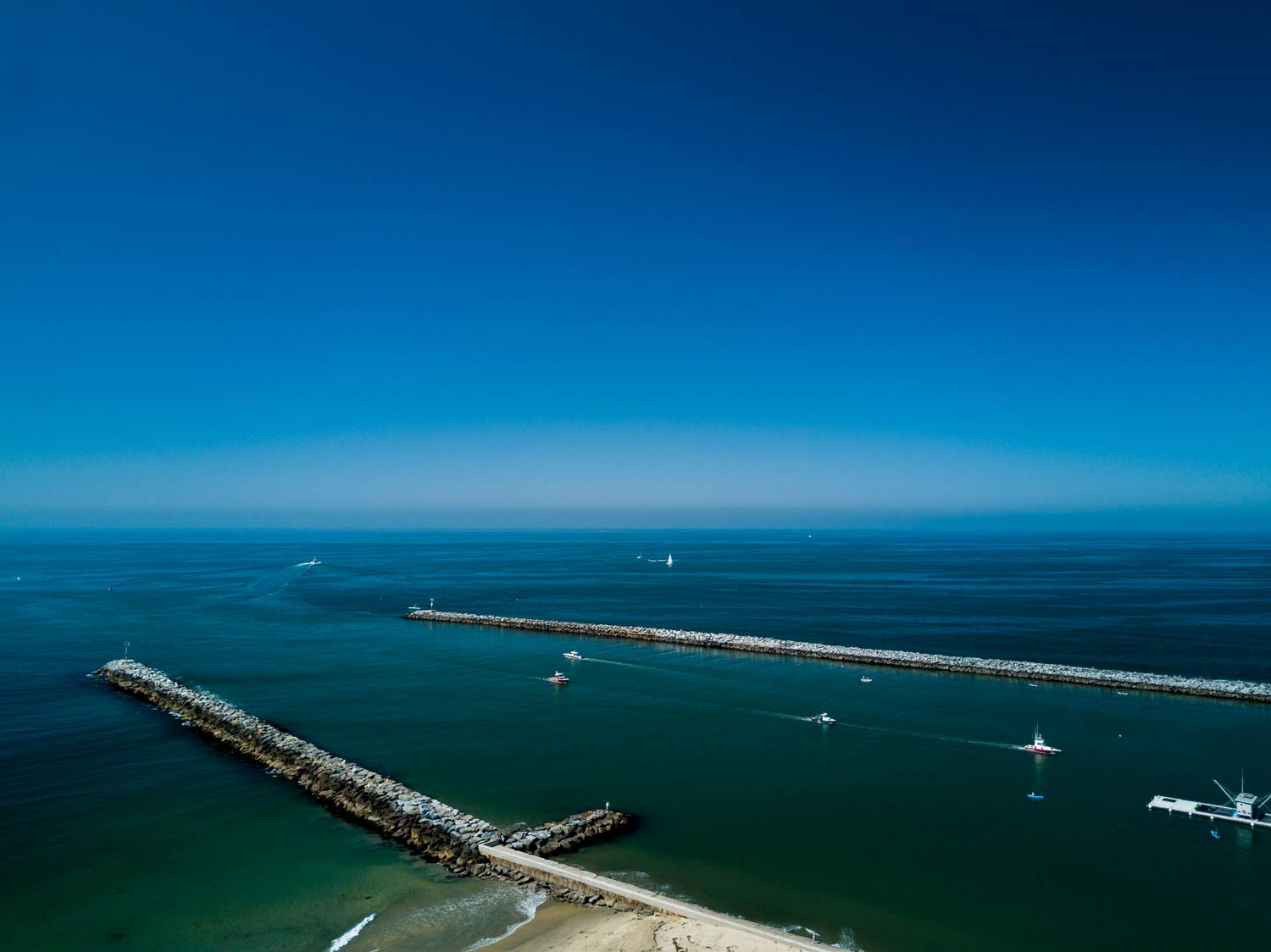 Aerial view of a beach and two long rock jetties extending into a calm blue ocean