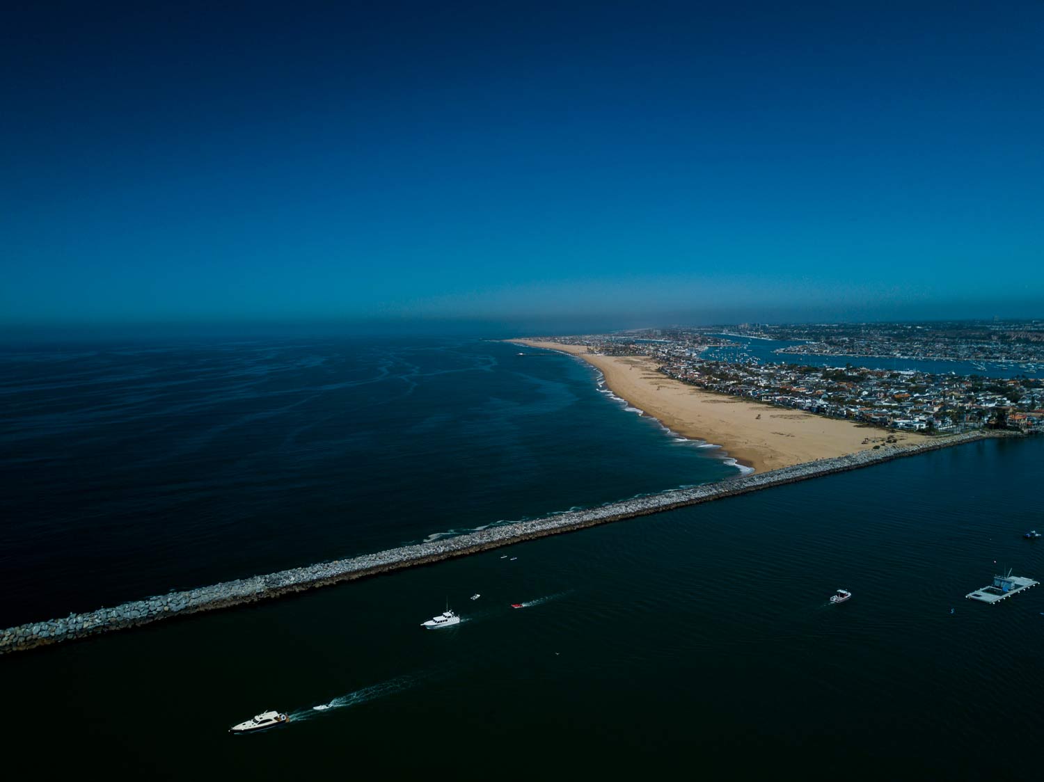 Aerial view of a long sandy shoreline with dark blue ocean and a city along the coast at dusk