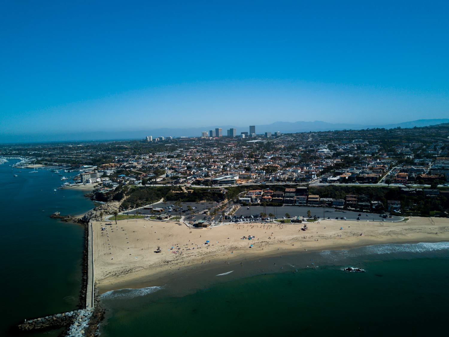 Aerial view of a sandy beach and coastal city skyline under a clear blue sky
