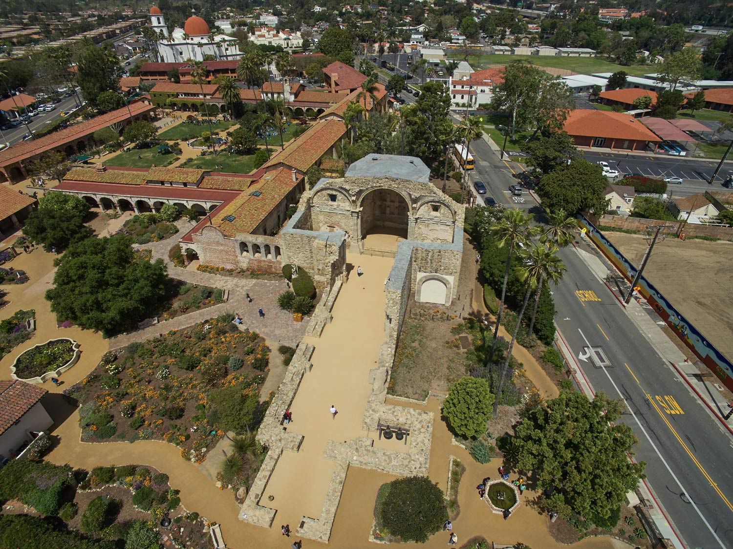 Aerial view of a historic stone site with courtyards, archways, and surrounding roads and trees.
