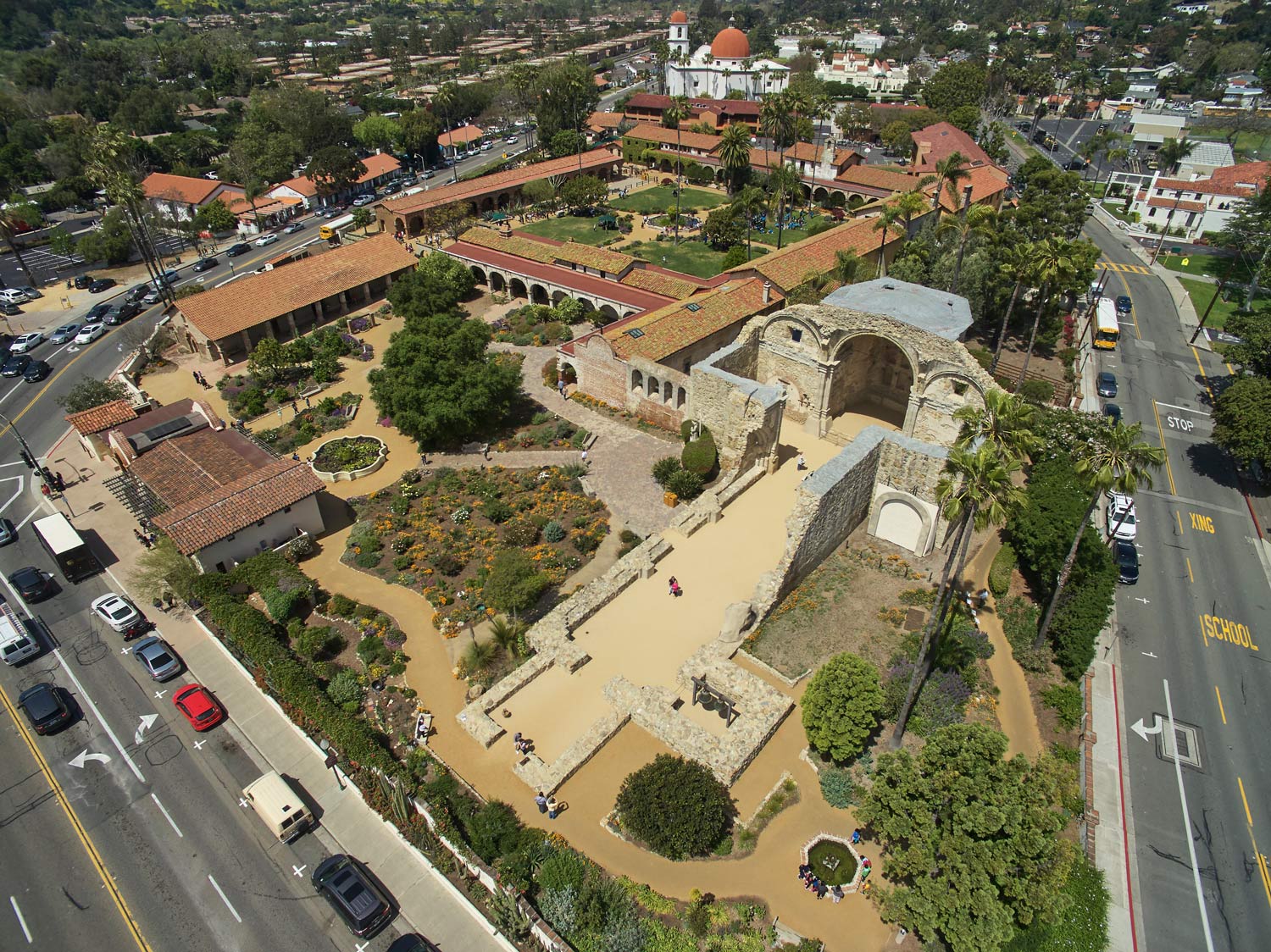 Aerial view of a historic building complex with courtyards, gardens, and adjacent roads in a city.