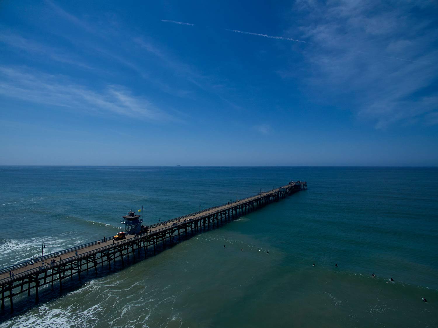 A long pier stretches into a calm blue ocean under a clear sky.