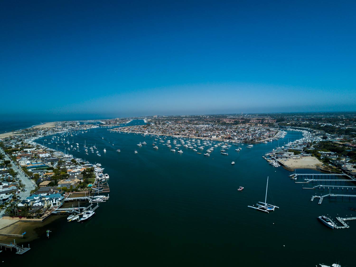 Aerial view of a wide blue harbor with boats and a city shoreline under a clear sky