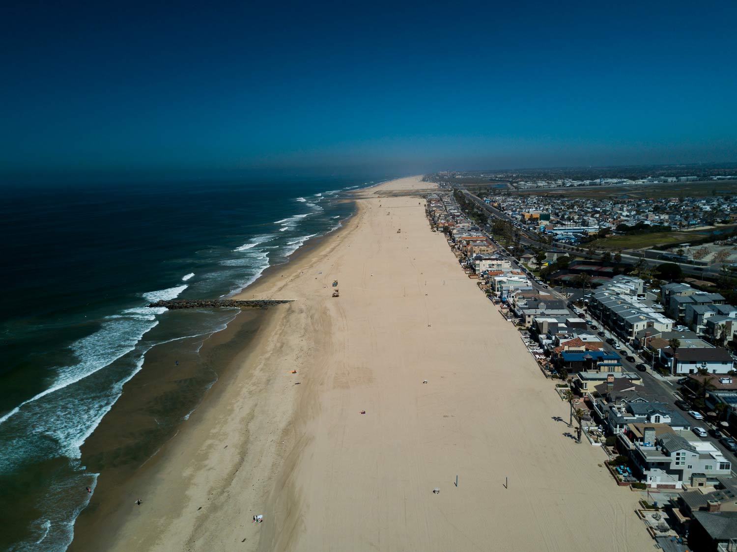 Aerial view of a wide sandy beach with ocean waves and a coastal neighborhood beside it