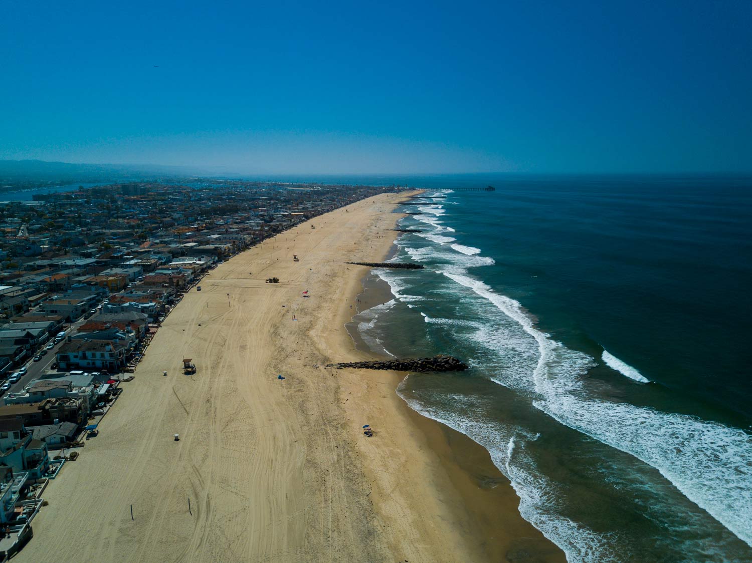 Aerial view of a sandy beach with ocean waves and a coastal city under a clear blue sky