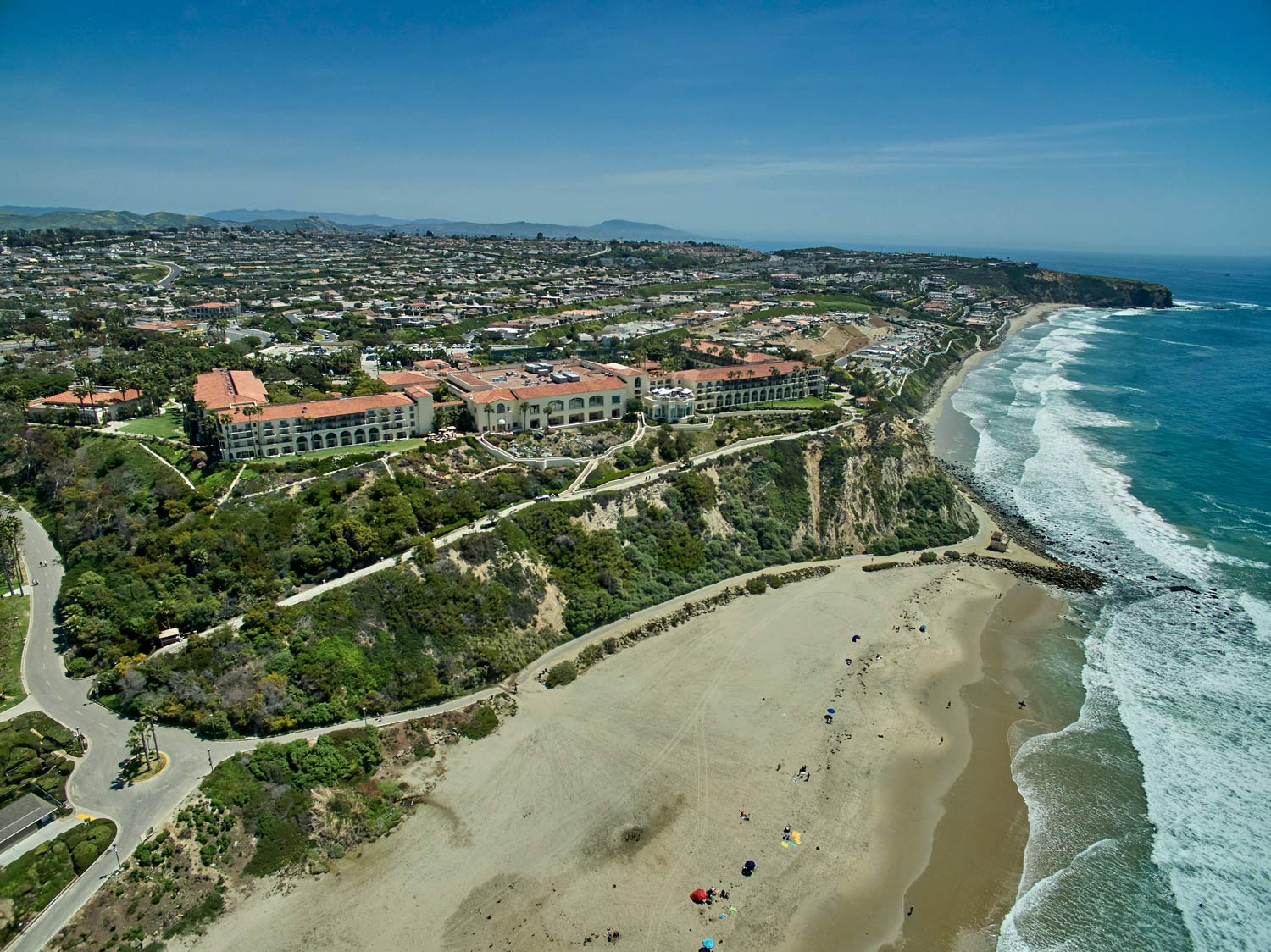 Aerial view of a coastal resort and beach with cliffs, houses, and waves along the shoreline