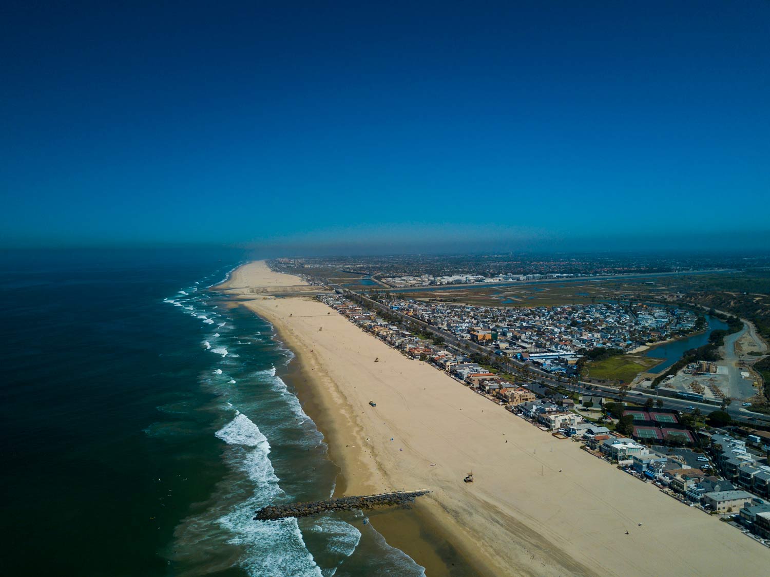 Aerial view of a long sandy beach beside blue ocean and a coastal town under clear sky