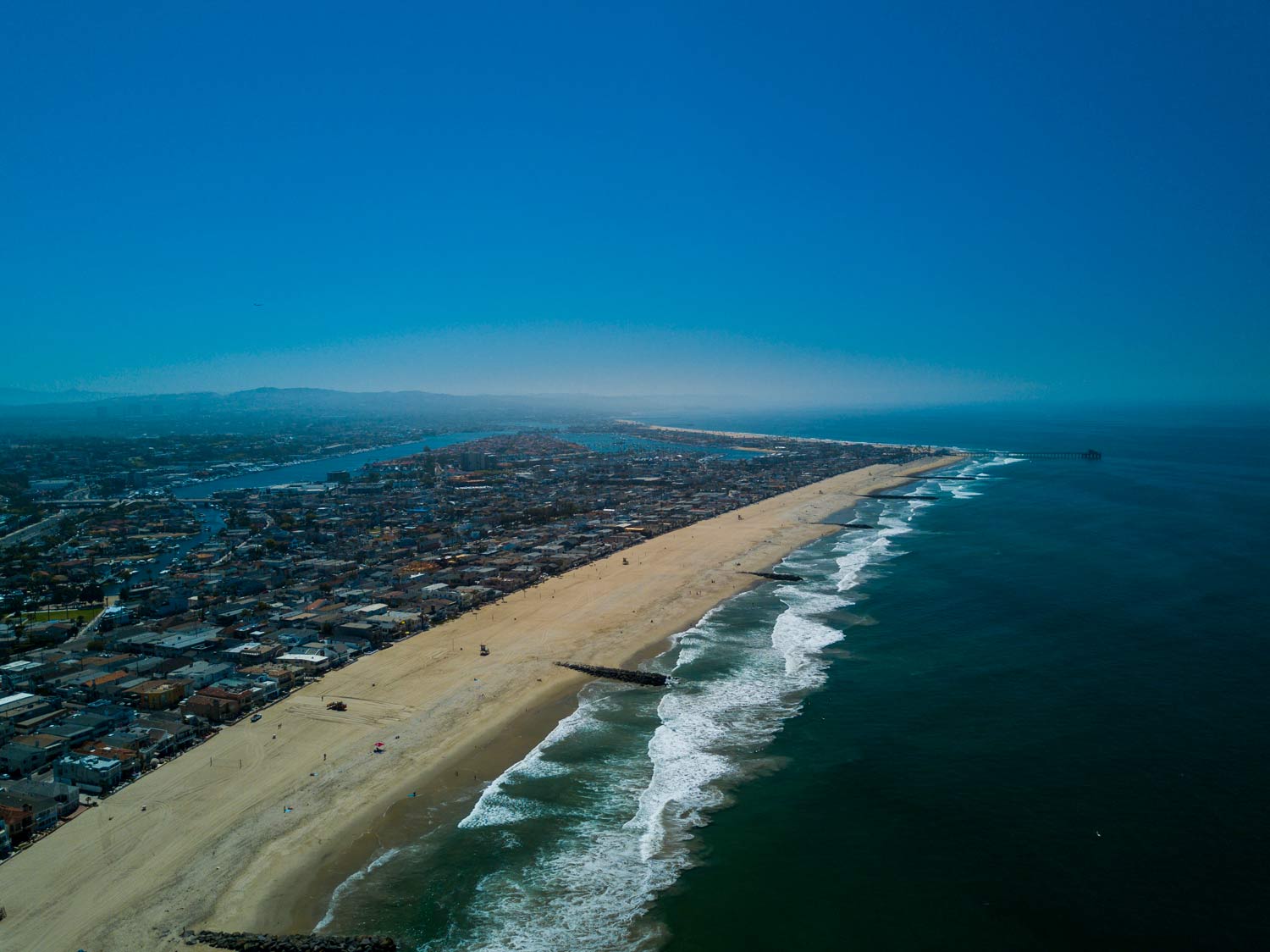 Aerial view of a sandy beach with waves on one side and a coastal city stretching inland.