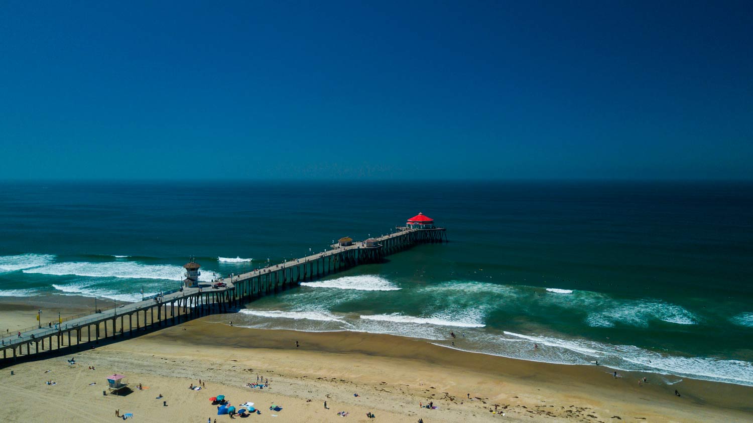 Long wooden pier extends from a sandy beach into the ocean under a clear blue sky.