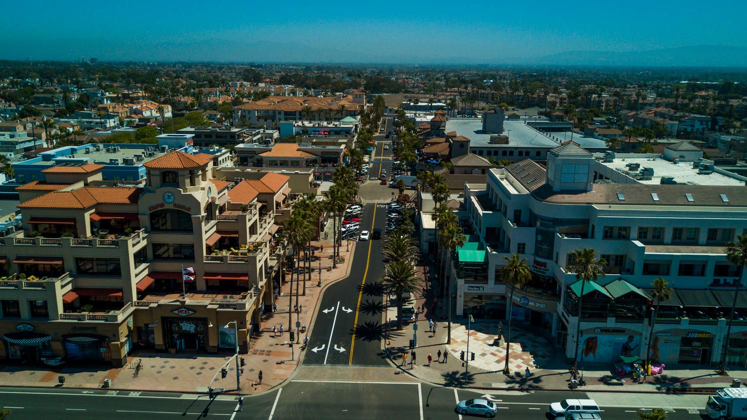 Aerial view of a busy downtown street lined with shops and buildings on a sunny day.